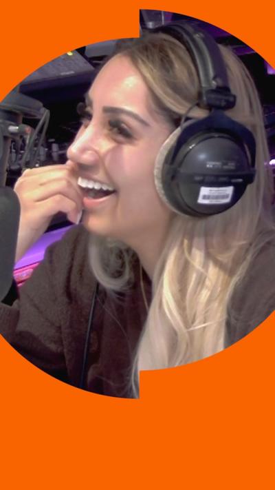 A woman with long blonde hair and headphones smiles in a radio studio