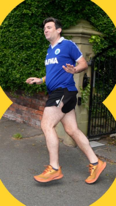 Andy Burnham wearing a blue t-shirt, black running shorts and orange trainers as he goes for a jog.