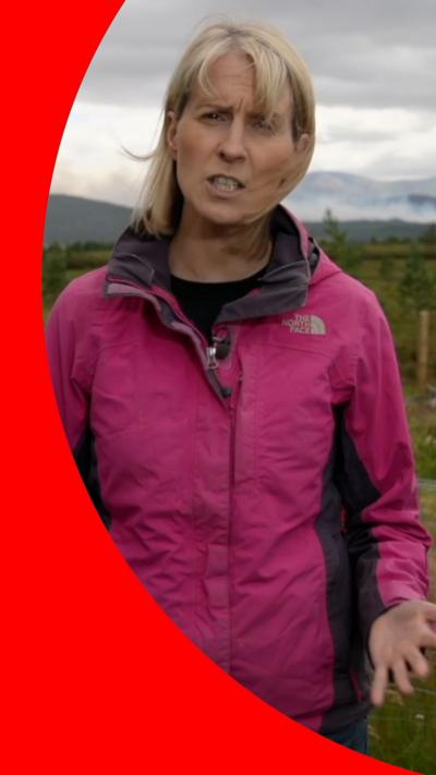 Katie Hunter wearing a pink windproof coat, as she speaks to camera in front of a cloudy sky.