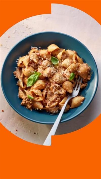 A blue bowl containing spiced beef pasta with grated cheese and basil leaves, with a fork sticking out of it 