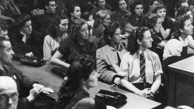 A crowd of mostly women sitting at long tables, looking up at a speaker who is out of view.