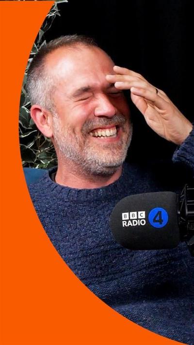 Dr Xand van Tulleken in a navy blue jumper on the What's Up Docs? podcast. He is laughing while speaking into a black mic that has the words 'BBC Radio 4' on it.