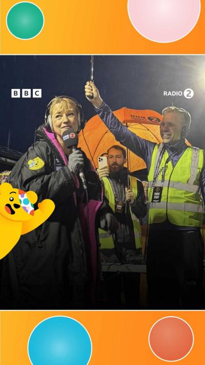 Sara Cox at the end of Day 1 of her challenge under an umbrella chatting on a Radio 2 mic