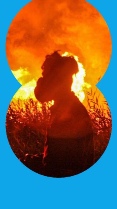 Silhouette of a person stood in front of a bushfire.
