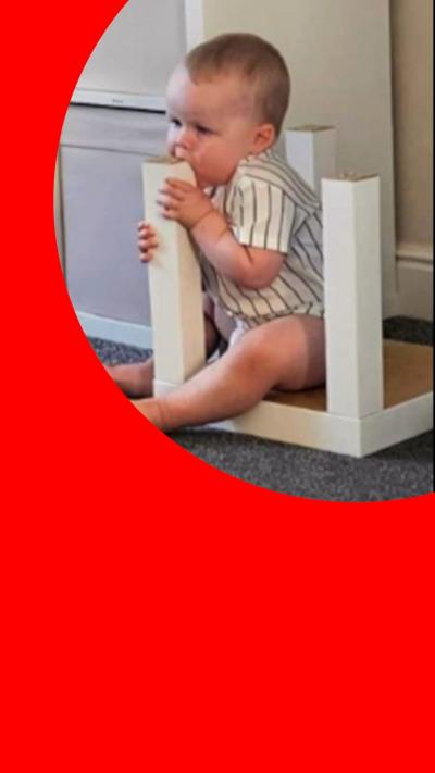 A toddler sits chewing the leg of an upside down table 