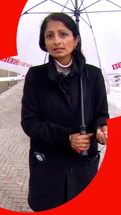 Reporter stands on the street holding an umbrella