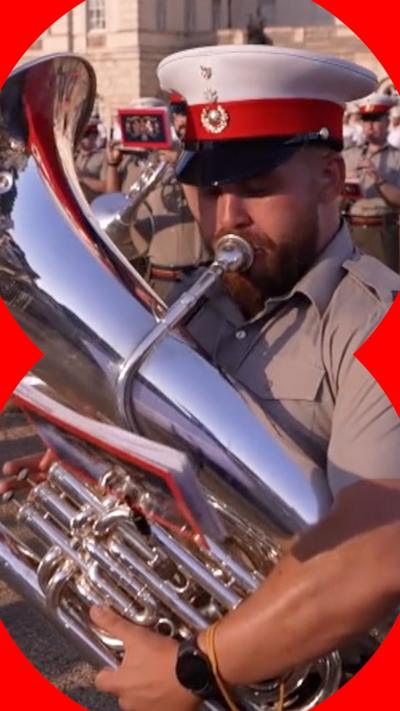 A marching band playing outside a building with a man playing a trombone in foreground