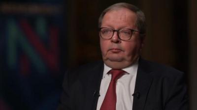 Andrei Kelin in a red tie sits in a dark room