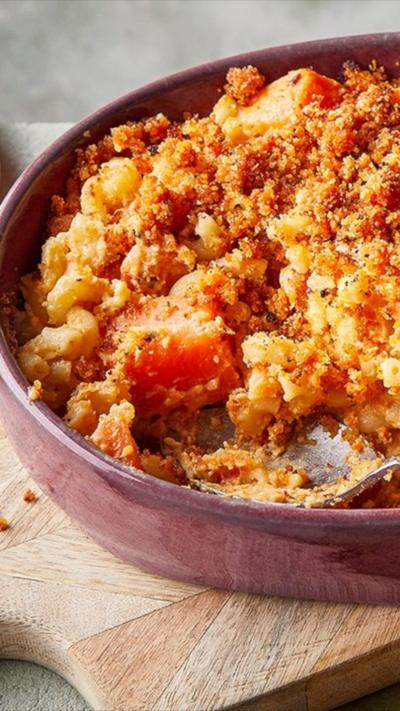 A pink bowl with mac and cheese and a crumbed topping. A spoon sits in the side.