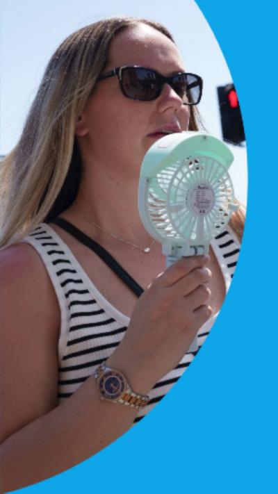 A woman cooling her face with a battery powered fan