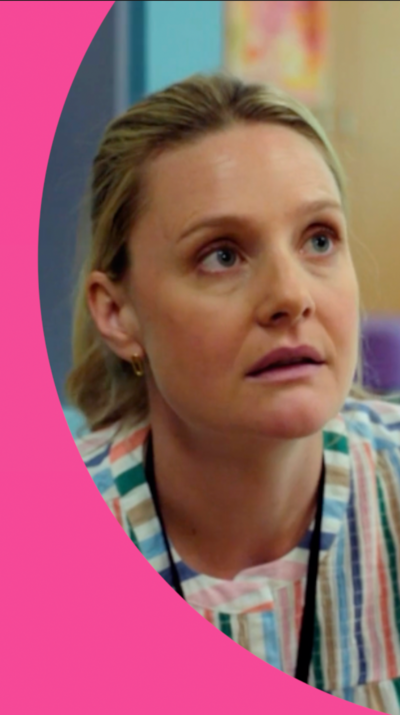 A female teacher in a striped top and lanyard kneeling down talking to a pupil