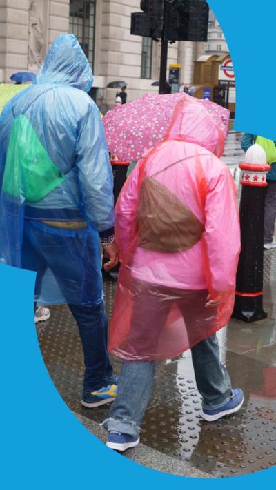 Two people seen from behind, one in a blue rain poncho and the other in a pink one.