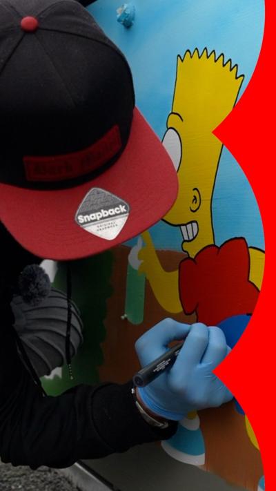 A person wearing a black and red cap uses a marker to draw on a colourful mural