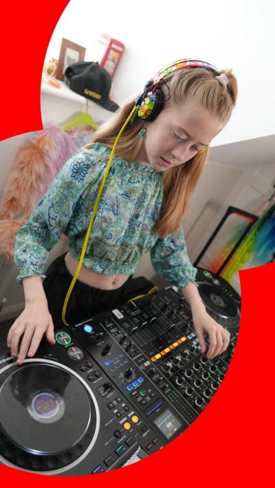 A young girl with rainbow headphones plays on DJ decks inside a house.