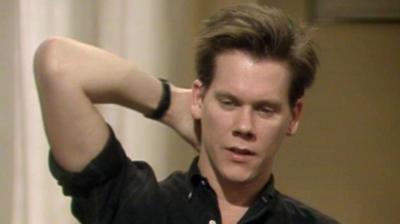 Kevin Bacon holds his hand behind his head.