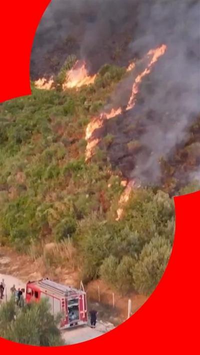 A grassy hill partially burned to black, with flames, and firefighter trying to control it. 