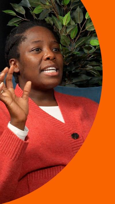 Woman in a red cardigan raising her hands whilst talking