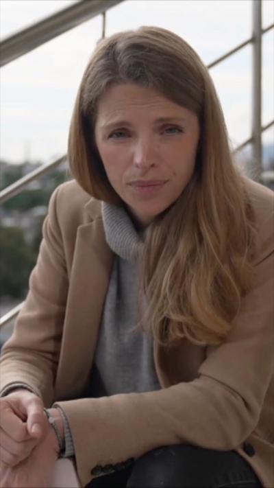 Carrie Davies, with long brown hair, dressed in beige jacket, looking at the camera