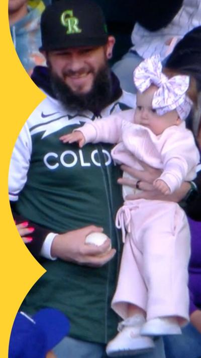 A man in a crowd holding a baseball in one hand and a baby in the other