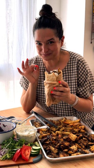 A woman gives the ok sign while holding a gyros. Two trays of food can be seen in front of her