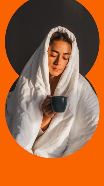 A woman with brown hair sits with her eyes closed and wrapped in a white duvet. Her eyes are closed and she is holding a black mug.