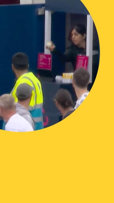 A woman catches a cricket ball in a popcorn stand while a crowd of people watch on