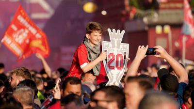 A young Liverpool fan holds up a cardboard cup with the number 20 on it.