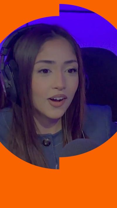 Duaa Karim has long dark brown hair. She is wearing a grey jacked buttoned up to the neck and sitting behind a microphone.