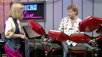 Leslie Judd standing beside drummer Bill Bruford, using a red electronic drum kit