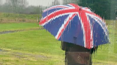 Person stands in rain holding a union flag umbrella