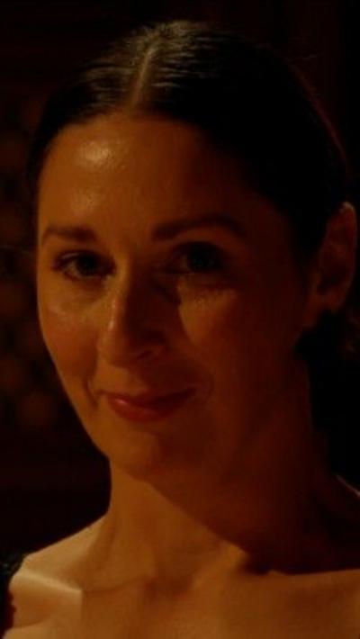 Rachel Duffy has long brown hair tied back. She is standing in a dark room.