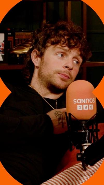 Tom Grennan looking to the right, speaking into a microphone