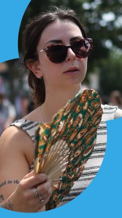 Woman in stripy top and sunglasses carrying a fan
