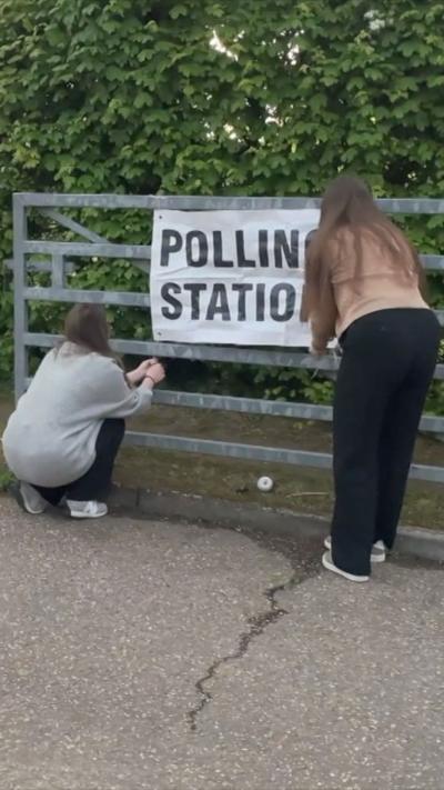 Polling station sign being put up on a metal gate. 
