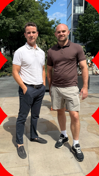 Two men stand in the street. One wears trousers, the other wears shorts