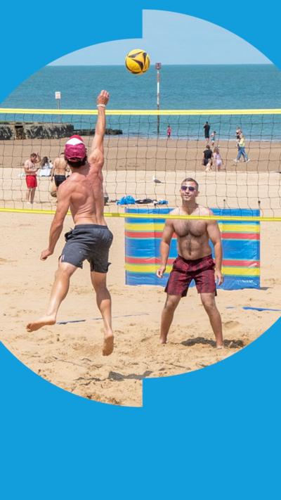 Two people playing beach volleyball. The sea is in the background.