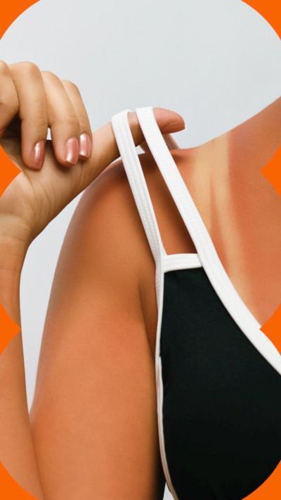 A woman lifts her black and white bikini strap off her shoulder to reveal a suntan mark.