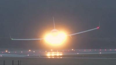 A plane attempts to land on a runway while it is tilted to the right with its left wing raised.