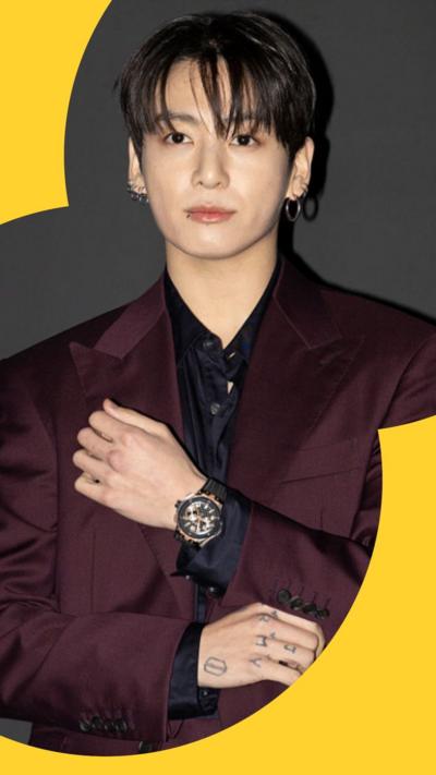Jungkook of BTS looks at the camera. They are wearing a burgundy suit. 