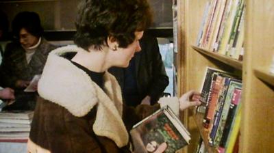 Woman in thick winter coat choosing books in a mobile library van.