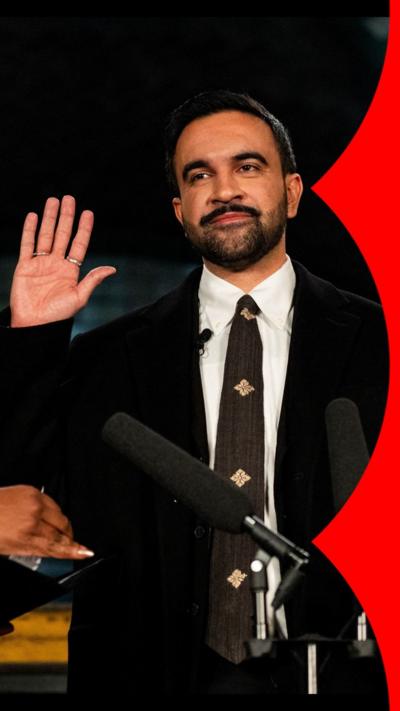 Zohran Mamdani holding his hand up