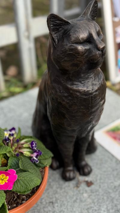 A black metal statue of a cat, sitting on a piece of granite beside a flowerpot.