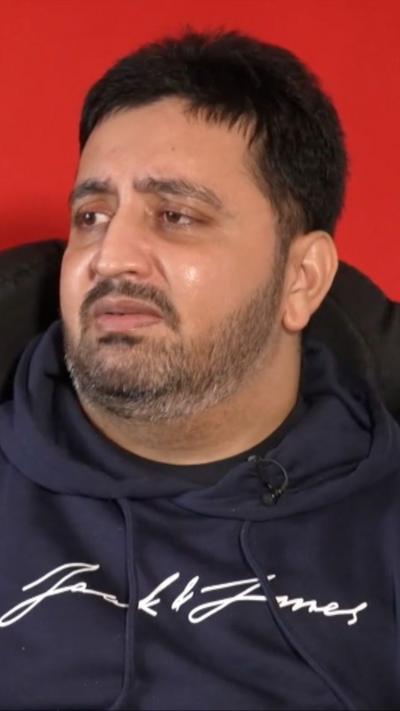 A man wearing a navy hoodie with writing on it, frowning at the camera