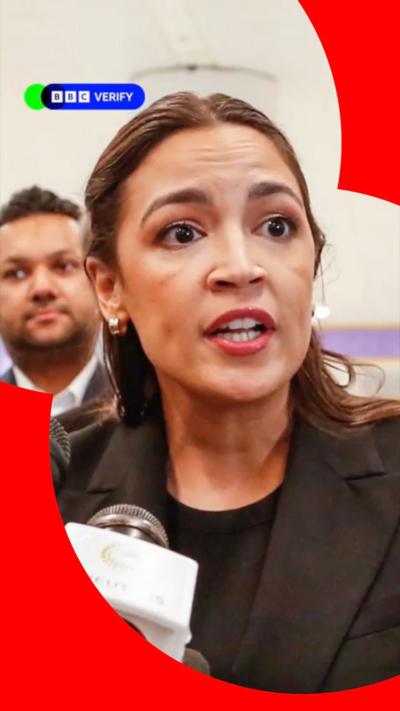 Alexandria Ocasio-Cortez speaking into a mic in front of a US flag