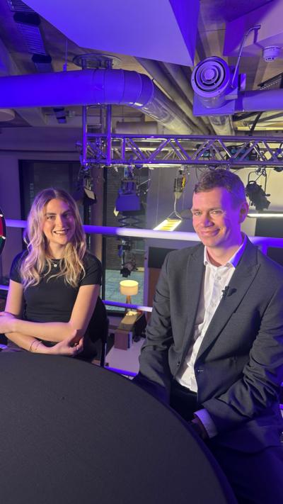 A female reporter and male reporter smile at the camera