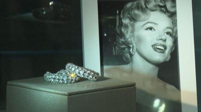 Sparkling earrings sit in a glass case in front of a portrait of Marilyn Monroe