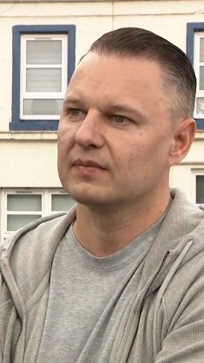 William Podwalski has short hair, shaved at the side, he wears a grey T-shirt and grey hoodie