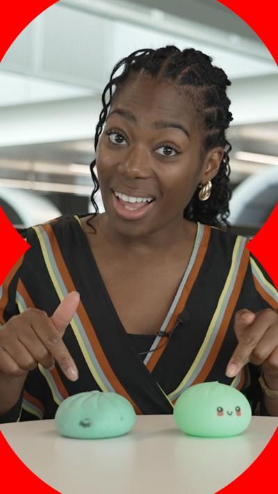 A woman with dark hair pulled back from her face points at two similar squishy toys on the desk in front of her