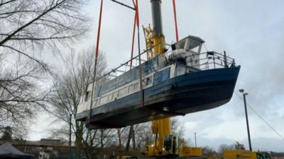 Blue and white boat lifted out of a river by a yellow crane