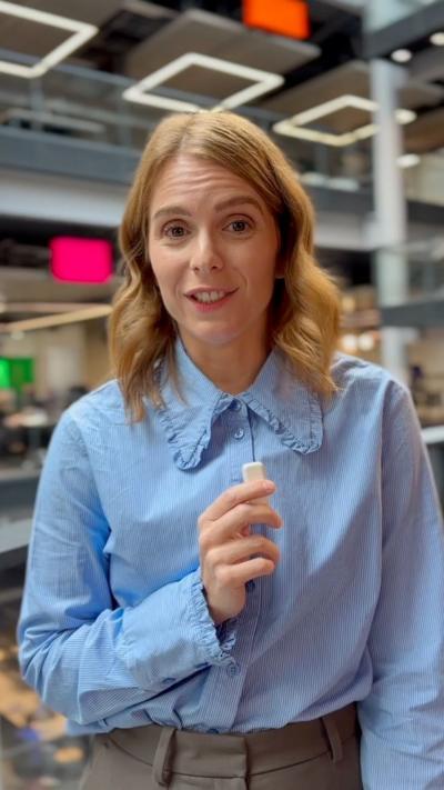 Kate Morgan, who has light brown hair, wearing a light blue buttoned up blouse and holding a microphone